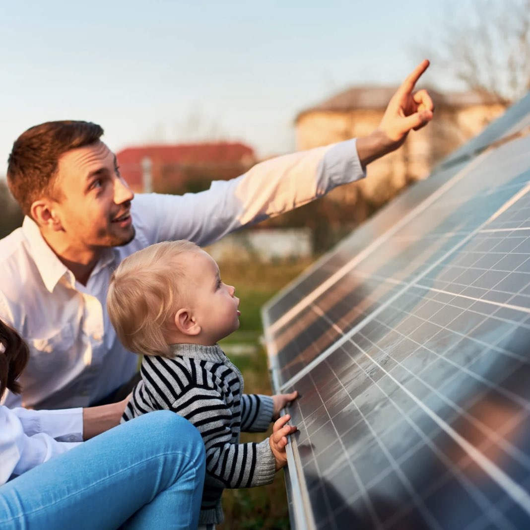 Vater und Kleinkind betrachten gemeinsam eine Solaranlage, während der Vater nach vorne zeigt.